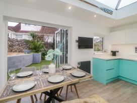 A dining table set for six with plates and glasses next to a turquoise kitchen and open folding doors to a garden at Ingledene in Brixham