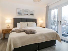 A bedroom with a bed with pillows and a blanket two bedside tables with lamps and a glass door at Ingledene in Brixham