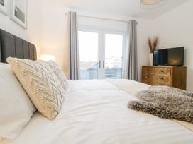 A bedroom with a bed a textured pillow a dresser with a television and glass doors with curtains at Ingledene in Brixham