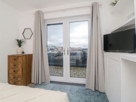 A bedroom with a wooden chest of drawers a plant a wall mirror curtains glass doors a blue rug and a television at Ingledene in Brixham