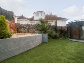 A backyard with artificial grass a concrete wall plants a stone wall and a dark wooden garden shed at Ingledene in Brixham