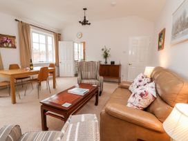 A living room with a brown leather sofa and striped armchair a wooden coffee table and dining table next to a window at 6 Granary Court in York