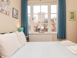 A bedroom with a bed, white pillows, folded towels, blue curtains, framed pictures, and a window showing a view of a cathedral and rooftops at 6 Granary Court in York