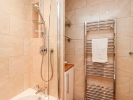 A bathroom with a shower, bathtub, chrome towel radiator with a white towel, and a cabinet with wooden countertop at 6 Granary Court in York