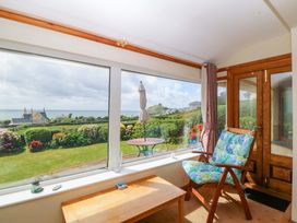 A sunroom with a chair and table overlooking the garden at Cwm Eilir in Criccieth