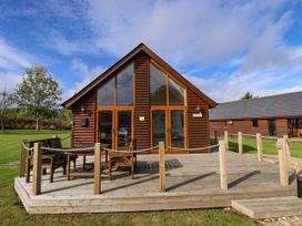 A wooden cabin with large glass doors and a deck with chairs and a table at Lodge 3 in Thorpe-On-The-Hill