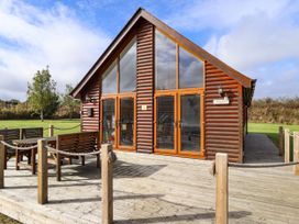 An outdoor wooden deck with a table and benches in front of a wooden lodge with large windows at Lodge 3 in Thorpe-On-The-Hill