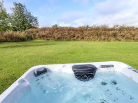 An outdoor hot tub filled with water on a grassy lawn with trees and bushes in the background at Lodge 3 in Thorpe-On-The-Hill