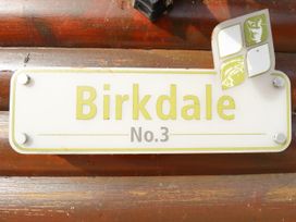 A white sign with green text reading Birkdale No 3 fixed to a wooden surface with a torn sticker in the top right corner