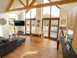 An open plan living room and kitchen with a gray sofa dining table wooden chairs and large windows at Lodge 3 in Thorpe-On-The-Hill