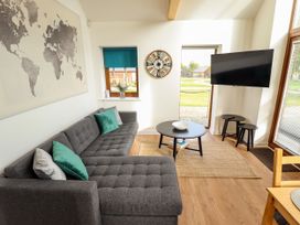A living room with a gray sectional sofa and green pillows a round black coffee table a wall clock a wall-mounted tv and windows at Lodge 3 Thorpe-On-The-Hill