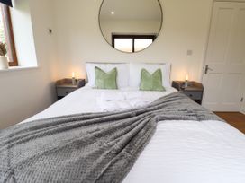 A bedroom with a bed with white bedding and green pillows two bedside tables with lamps a round mirror on the wall and a window at Lodge 3 in Thorpe-On-The-Hill