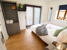 A bedroom with a bed with pillows and blankets a chest of drawers with towels a wall-mounted TV a mirror window with vases and sliding glass doors at Lodge 3 in Thorpe-On-The-Hill