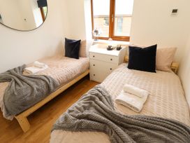 A bedroom with two single beds with beige bedding gray blankets and dark pillows with a white drawer and window in between at Lodge 3 in Thorpe-On-The-Hill