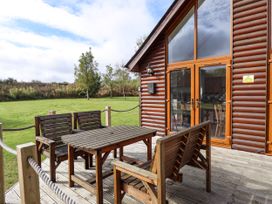A wooden deck with a table and chairs outside a log cabin with glass doors at Lodge 3 in Thorpe-On-The-Hill