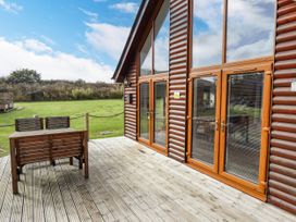 A wooden deck with a table and chairs outside a log cabin with large glass doors at Lodge 3 in Thorpe-On-The-Hill