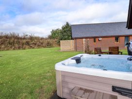 An outdoor area with a hot tub grassy lawn wooden chairs and a building with a slate roof at Lodge 3 in Thorpe-On-The-Hill