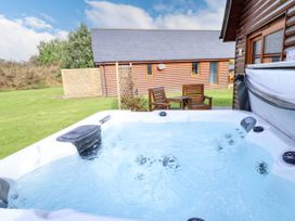 An outdoor hot tub with water in a garden near wooden chairs and a log cabin at Lodge 3 in Thorpe-On-The-Hill