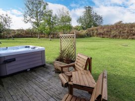 An outdoor deck with wooden chairs a planter with trellis and a hot tub with a grassy area and trees in the background at Lodge 3 in Thorpe-On-The-Hill