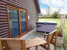 An outdoor wooden deck with a hot tub wooden chairs and a wooden lattice panel at Lodge 3 in Thorpe-On-The-Hill