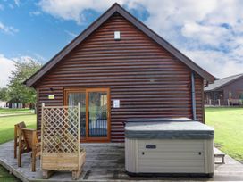 A wooden cabin with a hot tub and wooden chairs on a deck at Lodge 3 in Thorpe-On-The-Hill