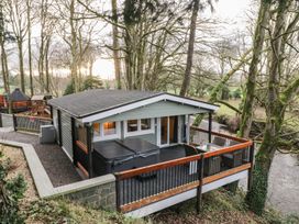 A cabin with a covered hot tub and outdoor seating on a deck overlooking a river surrounded by trees at Buttermilk Bridge in Dungiven