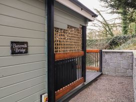 An outdoor area with a grey wooden wall and a sign reading Buttermilk Bridge next to a gravel path and wooden railing at Buttermilk Bridge in Dungiven