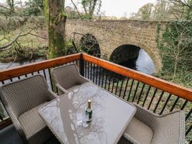 A balcony with a glass table and wicker chairs overlooking a stone bridge and river at Buttermilk Bridge in Dungiven