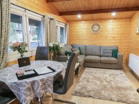 A living room with a grey sofa a round table with chairs flowers and windows at Buttermilk Bridge in Dungiven