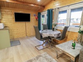 A dining area with a round table and four chairs next to large windows in a wooden room at Buttermilk Bridge in Dungiven