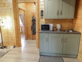 A small kitchen area with green cabinets a microwave a kettle and a sink in a wooden cabin at Buttermilk Bridge in Dungiven