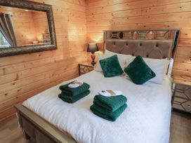 A bedroom with a bed with green pillows and towels on a white bedspread and wood paneled walls at Buttermilk Bridge in Dungiven