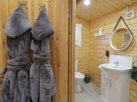 A bathroom with wooden walls a white sink a round mirror a toilet and two gray bathrobes hanging on hooks at Buttermilk Bridge in Dungiven
