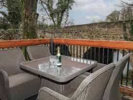 An outdoor seating area with a glass table four wicker chairs a bottle and two glasses near a stone wall at Buttermilk Bridge in Dungiven