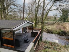 A deck with a hot tub and outdoor dining set next to a river surrounded by trees at Buttermilk Bridge in Dungiven