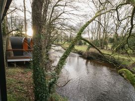 A river flowing beside trees with ivy and moss near two pod-like cabins at Buttermilk Bridge in Dungiven