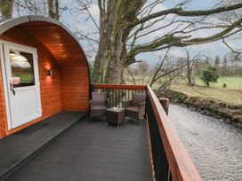 A wooden cabin balcony with two wicker chairs and a small table overlooking a river in a rural area at Pine in Dungiven Londonderry