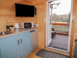 A kitchen corner with blue cabinets, microwave, kettle, a bottle, and a TV mounted on a wooden wall at Pine in Dungiven Londonderry