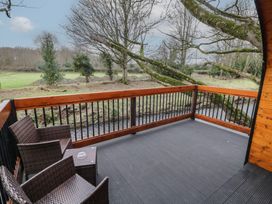A wooden deck with two wicker chairs and a small table overlooking a stream and trees at Pine in Dungiven Londonderry