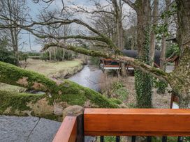 A wooden deck overlooking a moss-covered tree and a narrow river with houses and trees along the bank at Pine in Dungiven Londonderry