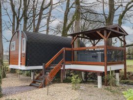 A small wooden cabin with black roof shingles on stilts next to a wooden deck with railing and stairs in a wooded outdoor area at Pine in Dungiven Londonderry