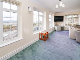 A living room with large windows a television on a stand a wooden nesting table and a sofa at Orme Villa in Llandudno