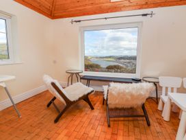 A room with two chairs covered in white fur, a wooden floor, a bench under a large window showing a coastal view at Orme Villa in Llandudno