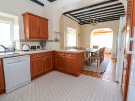 A kitchen with wooden cabinets a dishwasher and a dining area with a table and chairs at Orme Villa in Llandudno