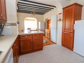 A kitchen with wooden cabinets white appliances and a dining area visible through an archway at Orme Villa in Llandudno