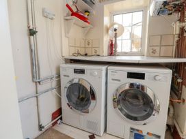 A laundry room with two front-loading washing machines under a countertop next to a window and pipes on the wall at Orme Villa in Llandudno