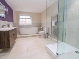 A bathroom with a freestanding bathtub a toilet a glass shower a wooden vanity with a sink and a purple accent wall at Orme Villa in Llandudno