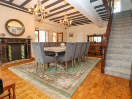 A dining room with a large table and gray chairs on a floral rug near a staircase and fireplace at Orme Villa in Llandudno