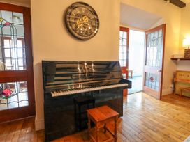A room with a black upright piano a wooden stool and doors with stained glass panels at Orme Villa in Llandudno