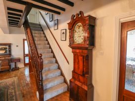 A staircase with carpet and wooden banister next to a wooden grandfather clock in a hallway at Orme Villa in Llandudno